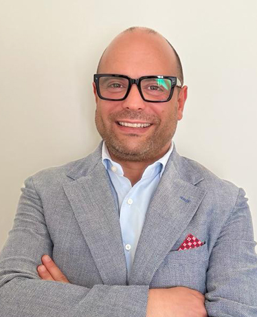 Ritratto in primo piano del consigliere comunale Michele Arcaini con occhiali da vista, giacca grigia e camicia azzurra.