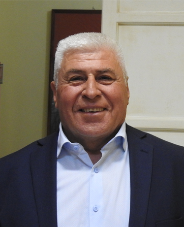 Ritratto in primo piano del consigliere comunale Valentino Quaranta, sorridente, con capelli bianchi, corti giacca scura e camicia azzurra.